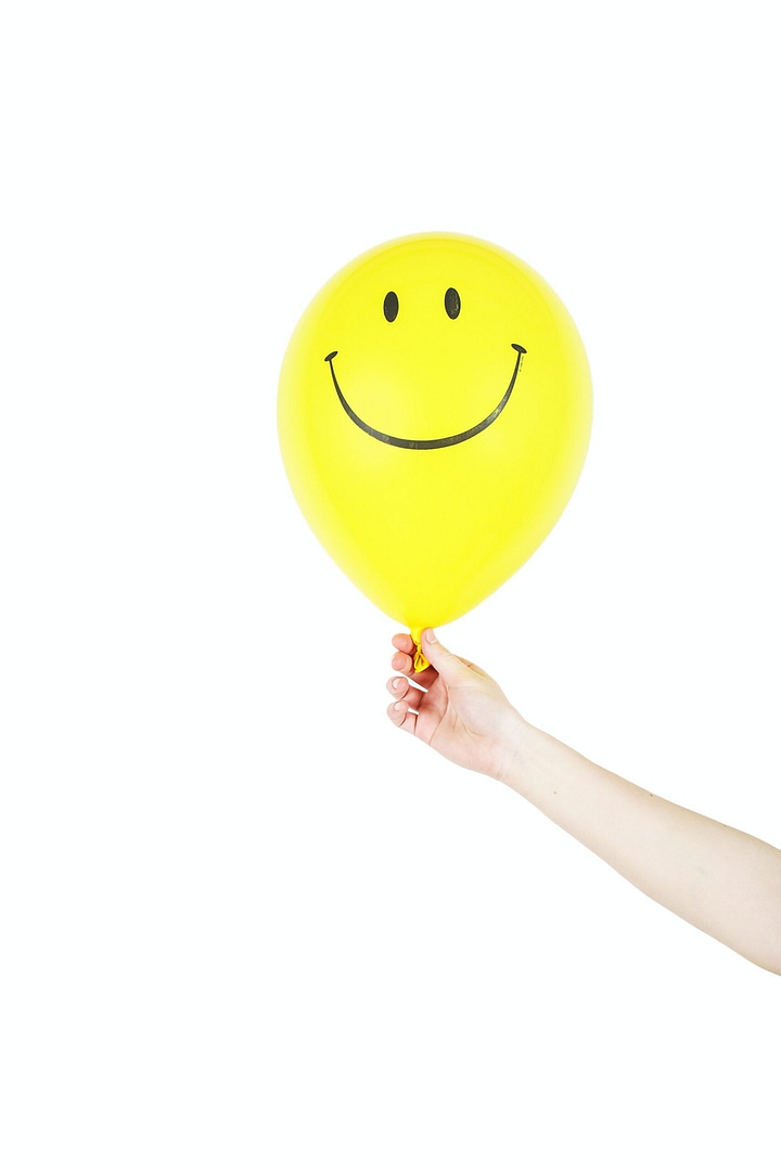 Person holding a yellow balloon with a smiley face drawn on it
